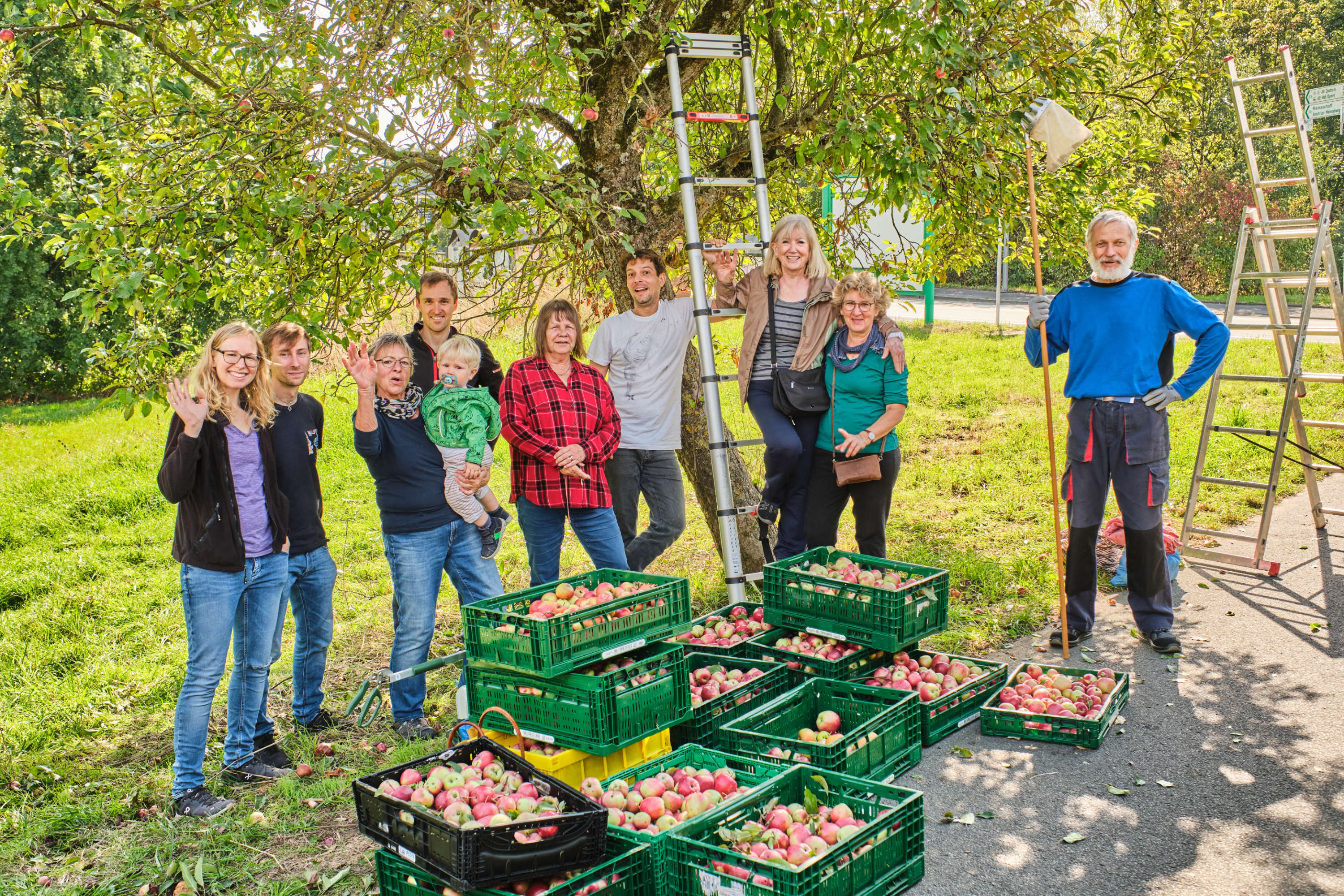 Ein Gruppenfoto von Menschen, die bei der Ernteaktion 2023 geholfen haben. Im Hintergrund ist ein Apfelbaum zu sehen, im Vordergrund Kästen mit den geerntete Äpfeln. Die Menschen haben Geräte zur Apfelernte in den Händen.